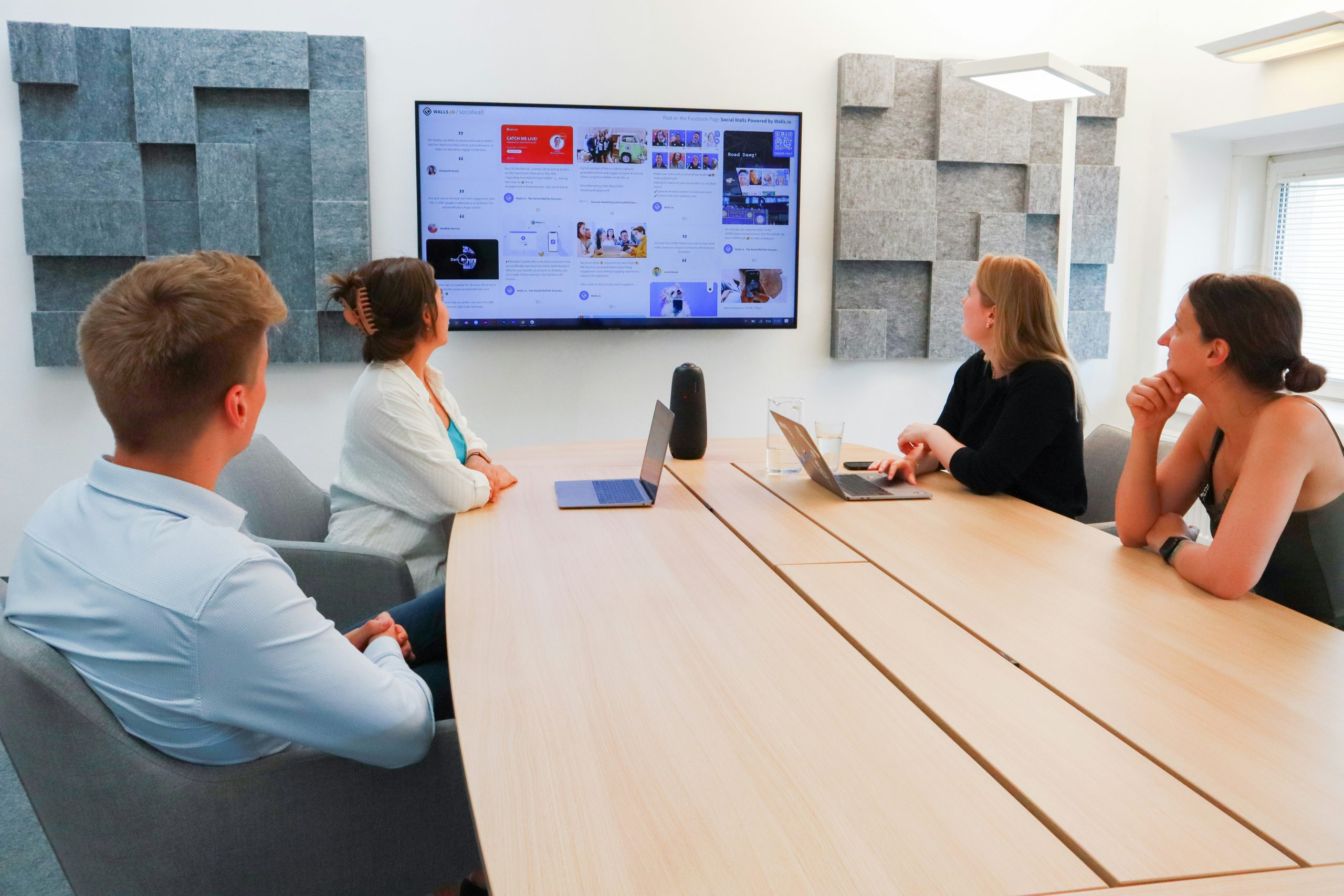 Team members collaborating in a modern meeting room, viewing a presentation on a large screen, with laptops and a creative workspace atmosphere.