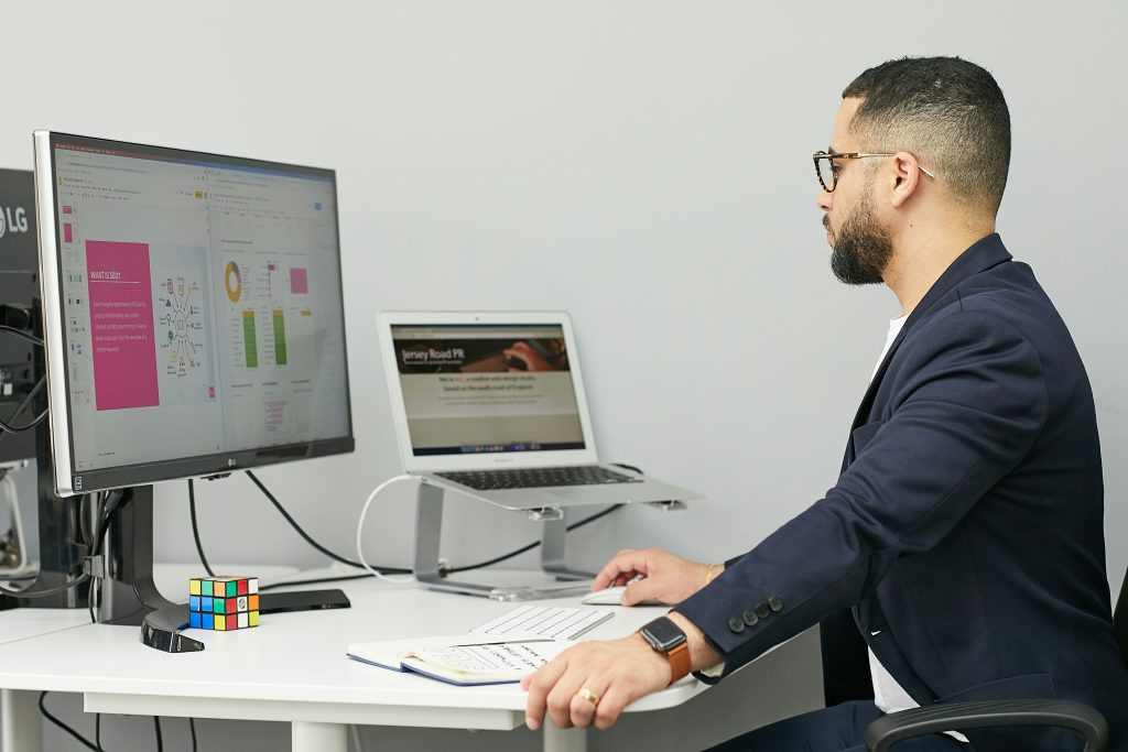 Man working at a desk with dual monitors displaying digital marketing analytics and design concepts, highlighting a professional web development environment.
