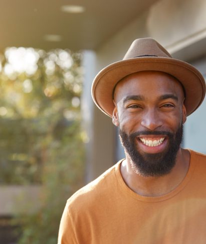 Smiling African American man in a brown hat and orange shirt, embodying a friendly and approachable demeanor, reflecting the innovative and client-focused spirit of Adonis Designs.